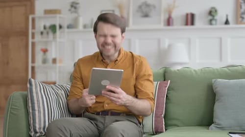 Man Celebrating Success While Using Tablet at Home