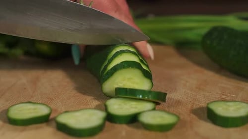 Closeup of Woman Cutting Fresh Cucumbers on a Wooden Board on a Black Background