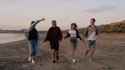 Full Length Shot of Young People Running Along Seaside with Young Girl Turning and Trying to Run