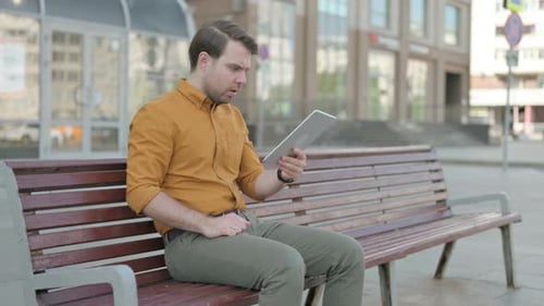 Man Frustrated While Using Tablet on Bench