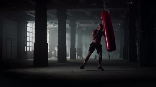 Muscular Man Punches Heavy Bag in Industrial Gym