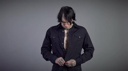 Tattooed Man Buttoning Black Shirt in Studio