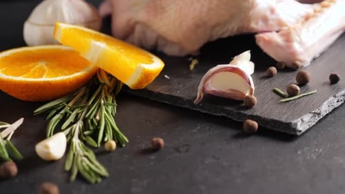 Raw Organic Whole Duck with Cut Orange and Rosemary on Slate Board on Black Background
