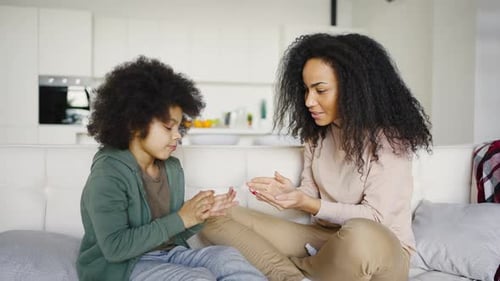 Une jeune maman métisse et son fils traitent les mains avec un spray antiseptique tout en étant assis sur le canapé à