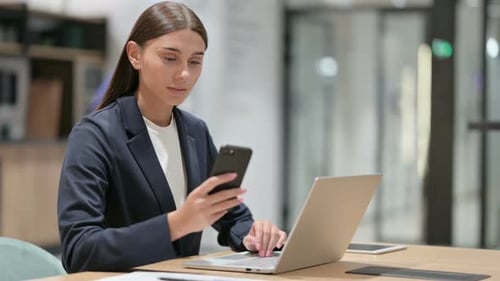 Disappointed Businesswoman Using Smartphone and Laptop in Office