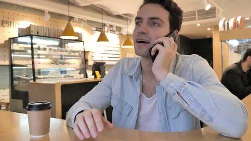 Young Man Talking on Phone Sitting in Cafe