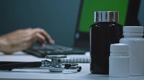 The doctor works at the computer in his office. Hands close-up typing