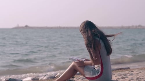 Langhaarige Brünette liest ein Buch am Ozeansandstrand
