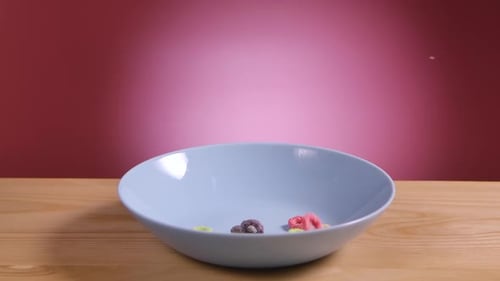 Breakfast Cereal in Form of Multicolored Corn Rings Fall and Fill White Bowl on Table