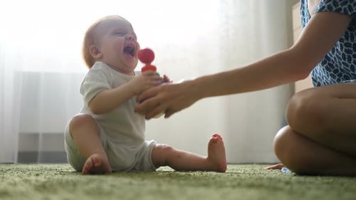 Red-Haired Baby Plays with Toy Rings with Mom