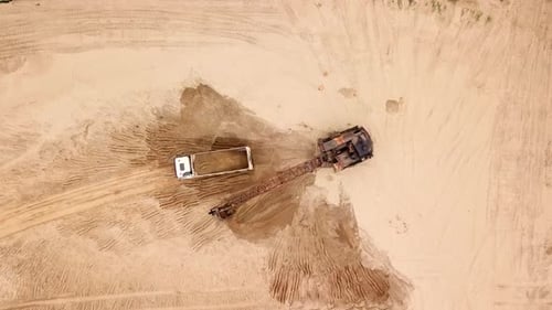 Top Down View of Excavator Pours Sand Into the Truck, Near the Trees. On the Construction Site