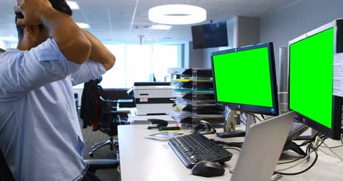Stressed Man at Desk with Dual Green Screens
