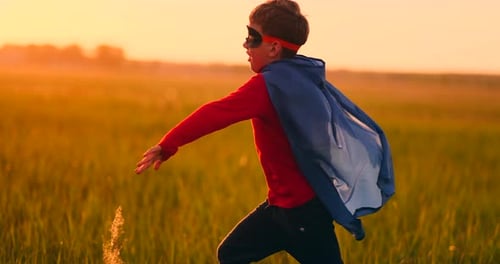 A Boy in a Superhero Costume at Sunset Runs Across the Field Laughing and Smiling