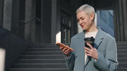 Smiling Woman Using Cell Phone and Holding Coffee on Street