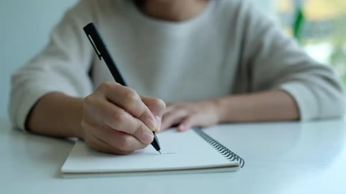 Person Writing in Notebook with Black Pen