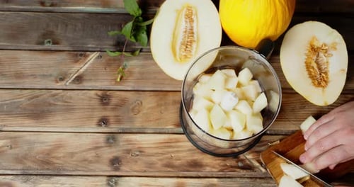 Mains mâles tranchant un melon en morceaux et les mettant dans un mixeur