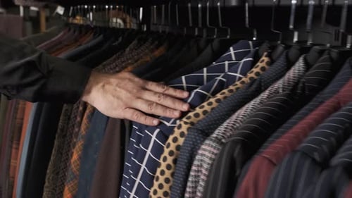 Male Hand Stroking Suits on a Hanger in a Store. Choosing a Jackets in a Tailor Shop