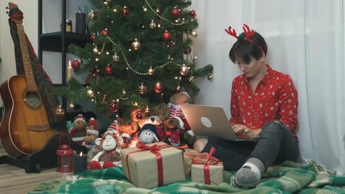 Charmante festliche junge Frau arbeitet zu Weihnachten oder Neujahr am Laptop.
