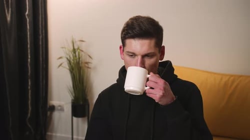 Man Enjoys Drink From Mug Indoors
