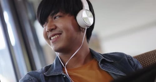 Happy young Asian man listening for music with headphone in living room.