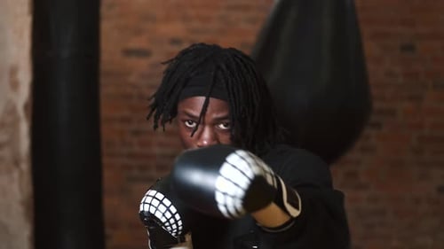 Dedicated Young Man Punching Boxing Bag at Gym
