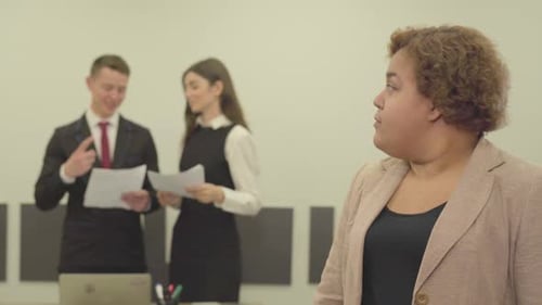 Portrait of Plump Woman in Formal Wear Looking in the Camera in the Foreground in the Office While
