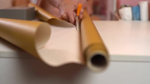 Closeup Front View of Unrecognizable Young Woman Cutting with Scissors Wrapping Golden Paper to