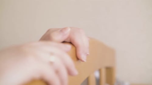 Woman's Hands Gently Resting on Wooden Baby Crib