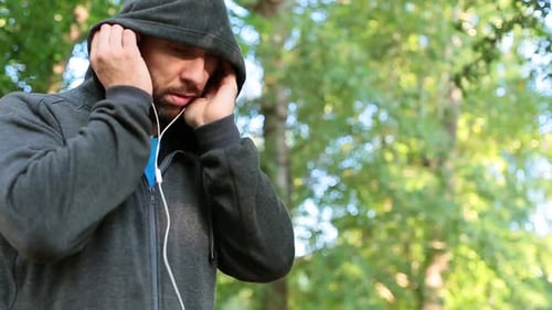 Man in Hooded Sweatshirt Listens to Music and Jogs