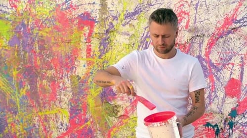 Man Stirring Paint in Front of Colorful Wall