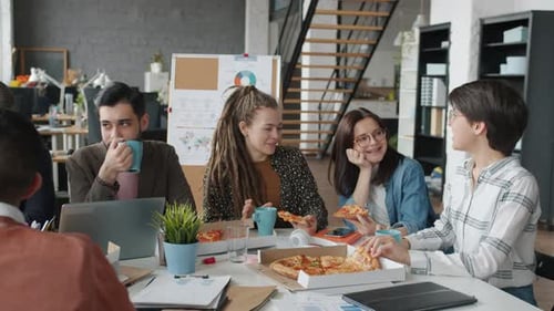 Group of Men and Women Eating Pizza Talking and Laughing in Open Space Office