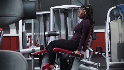 Uma mulher negra malhando em uma academia com um equipamento de exercícios para as pernas
