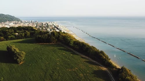 Drone Rising Above Green Tree Mountain Hill with Epic Sea View To Reveal Small Sunny Bay Town