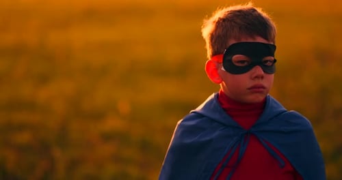 The Boy in the Mask and Cape of a Super Hero at Sunset in a Field