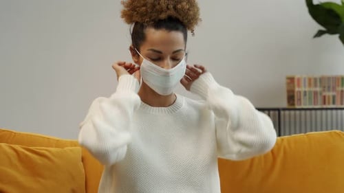Woman Puts on Face Mask on Yellow Couch