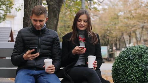 Freunde surfen im Internet, trinken Kaffee und reden, während sie auf einer Bank auf der Straße sitzen