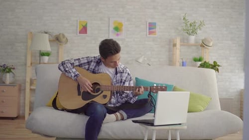 Young Adult Playing Guitar at Home on Couch