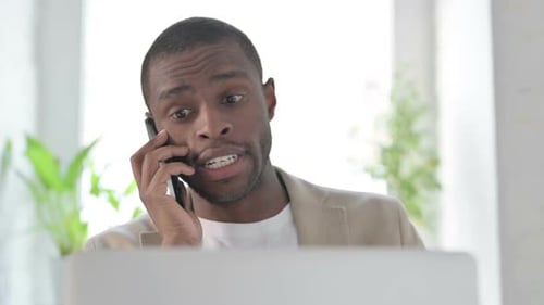Close Up of African Man with Laptop Talking on Smartphone
