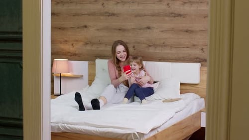 Mother and Daughter Using Smart Phone on Bed