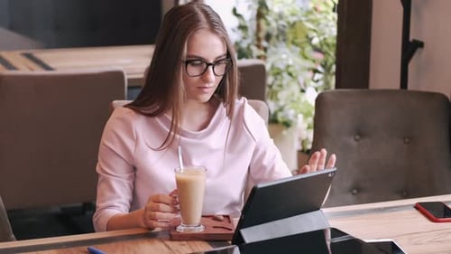Woman Working on Tablet in Coffee Shop with Latte