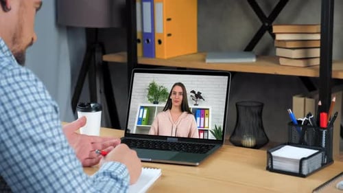 Man on Video Call Taking Notes at Desk