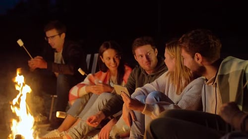 Friends Gathered Around Campfire at Night Roasting Marshmallows