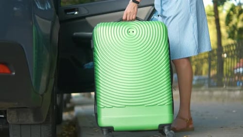 Young Woman Driver Taking Out Green Suitcase From Car on City Street