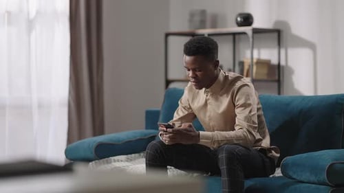 Young Adult Using Smartphone on Couch at Home
