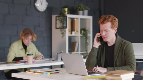 Man Talking on Phone Working at Laptop in Office