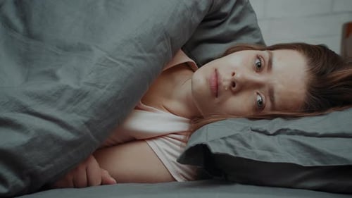 Femme malheureuse pleurant en regardant la caméra allongée dans son lit à l'intérieur