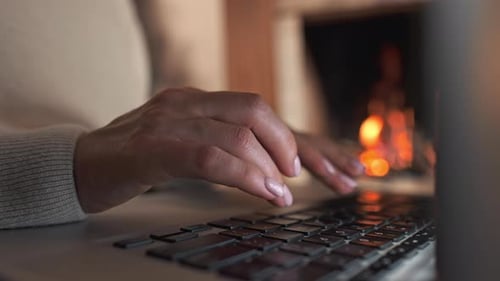 Woman Typing on Laptop by Fireplace