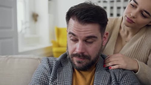 Bearded Man which Sitting on the Sofa and His Attractive Considerate Wife Trying to Calm Him
