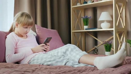 Young Girl Uses Phone Reclining on Bed
