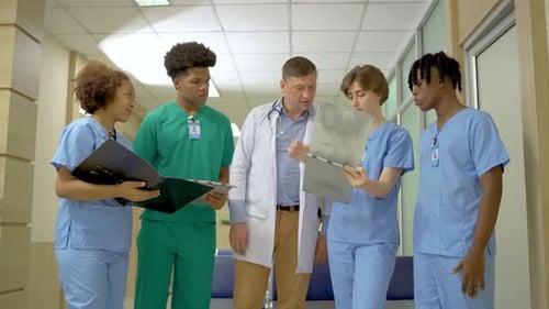 Male Doctor and Young Medical Interns have a discussing over documents in the hospital together